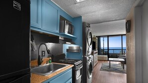 Una cocina compacta con armarios azules, un refrigerador negro, una estufa y una lavadora.