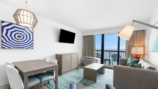 A modern hotel room with a dining area, a sofa, a TV, and a balcony with a view. - Unparalleled Oceanfront Luxury 6th Floor (Myrtle Beach)