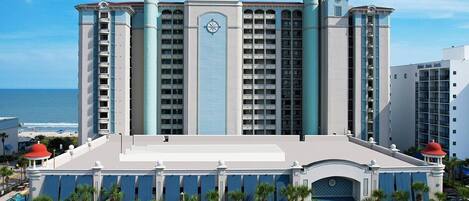 A large hotel with multiple floors, a prominent clock tower, and a view of the ocean.