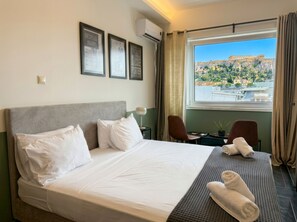 Habitación de hotel con una cama grande, un escritorio, dos sillas, una ventana con vistas a un edificio histórico y cuadros en la pared.