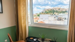 A room with a view of a historic hilltop, a small table with chairs, and a black console table with decorative items.