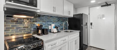 Una cocina moderna con gabinetes blancos, una estufa negra, un microondas y un refrigerador negro.