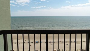Vue sur la plage depuis un balcon doté d’une balustrade, avec une plage de sable et l’océan en toile de fond.