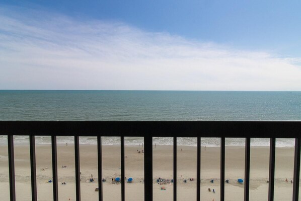 A beach view with a clear sky, calm sea, and a sandy shore with umbrellas and people.