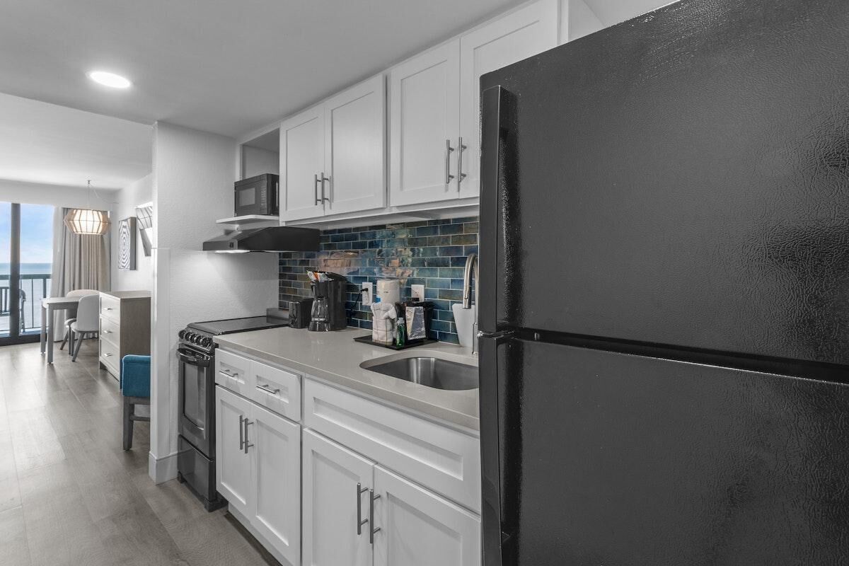 A modern kitchen with white cabinets, a black refrigerator, and a blue-tiled backsplash.