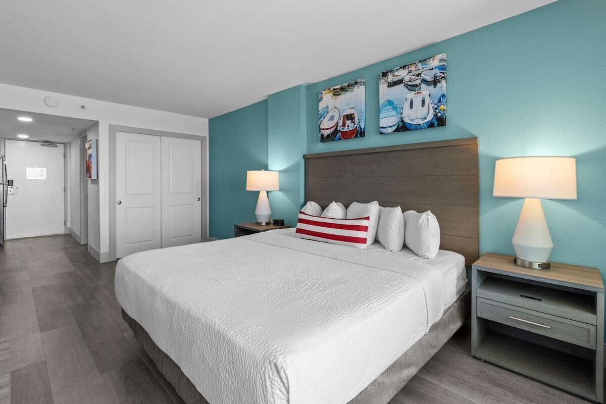A hotel room with a large bed, two bedside tables with lamps, a headboard, and artwork on the wall.