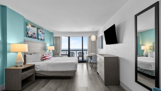A modern hotel room with a large bed, a desk, a chair, and a TV mounted on the wall.