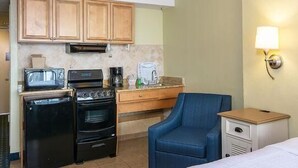 A compact hotel room with a kitchenette including a stove, microwave, and coffee maker. There is a single blue chair and a small bedside table with a lamp. - Calming Ocean View King Bed Accessible 4th Flr (Myrtle Beach)