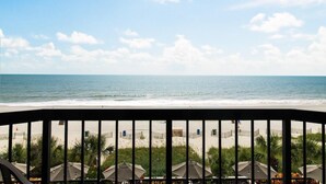 A beach view from a balcony with a railing, palm trees, and beach umbrellas. - Calming Ocean View King Bed Accessible 4th Flr (Myrtle Beach)
