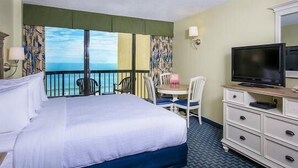Habitación de hotel con cama, televisor, cómoda, escritorio con silla y vista al océano.