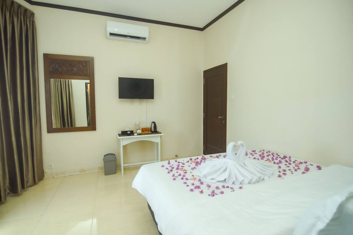Una camera d'albergo con un letto, una TV, un condizionatore, una scrivania con un bollitore e una porta.