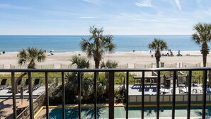 A beach view from a balcony with a pool and lounge chairs.