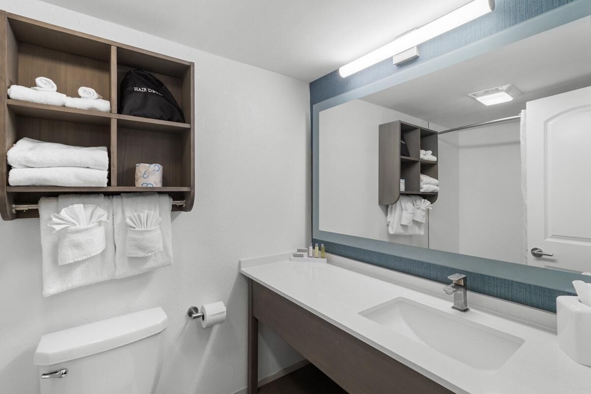 A modern bathroom with a large mirror, white sink, and towel storage.