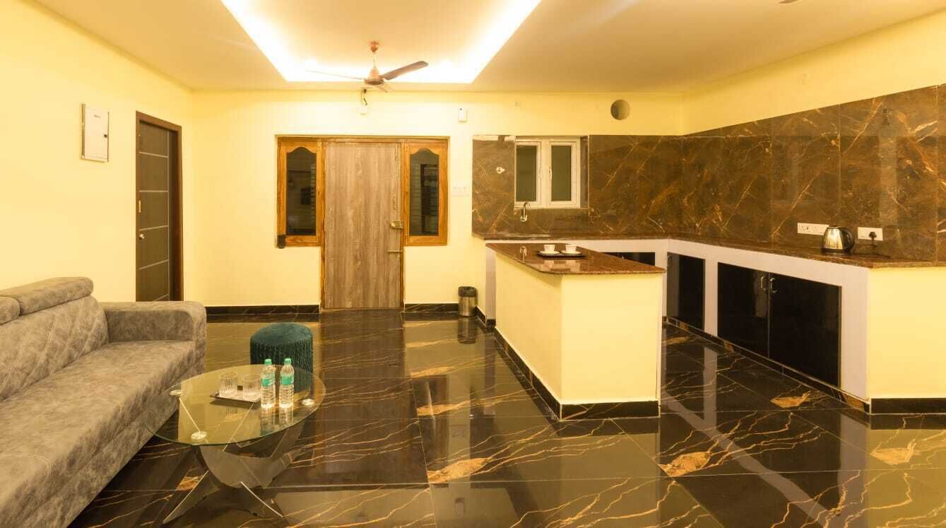 Una sala de estar moderna con un sofá, una mesa de centro de vidrio y una cocina con encimera de mármol y armarios negros.