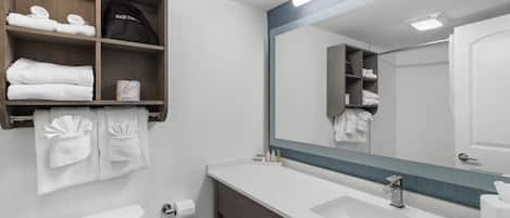A modern bathroom with a large mirror, white sink, and towel storage.