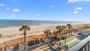 Vue sur la plage depuis un balcon, avec une piscine et des chaises longues.