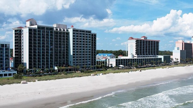 A beachfront hotel with multiple high-rise buildings, a sandy beach, and ocean waves. - Dreamy Getaway Oceanfront Cabana Room 4th Flr (Myrtle Beach)