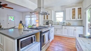 A modern kitchen with white cabinetry, a large island with appliances, and a ceiling fan. - Comfortable Downtown Napa Victorian - quiet & convenient
 (Napa)