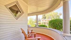 A covered porch with wooden chairs, a small window, and a view of greenery and buildings. - Comfortable Downtown Napa Victorian - quiet & convenient
 (Napa)