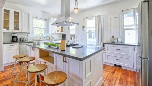 A spacious kitchen with white cabinetry, a large island with stools, and a stainless steel range hood. - Comfortable Downtown Napa Victorian - quiet & convenient
 (Napa)