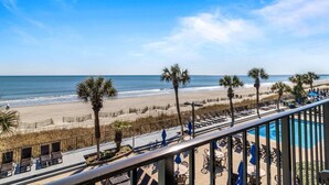 Un balcon avec vue sur une plage, des palmiers et un espace piscine.