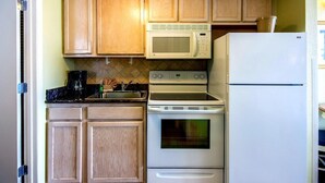 Una cocina compacta con armarios de madera, un microondas, una estufa y un refrigerador.