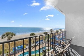 Un balcón con vistas a la playa, la piscina y sillas de descanso.