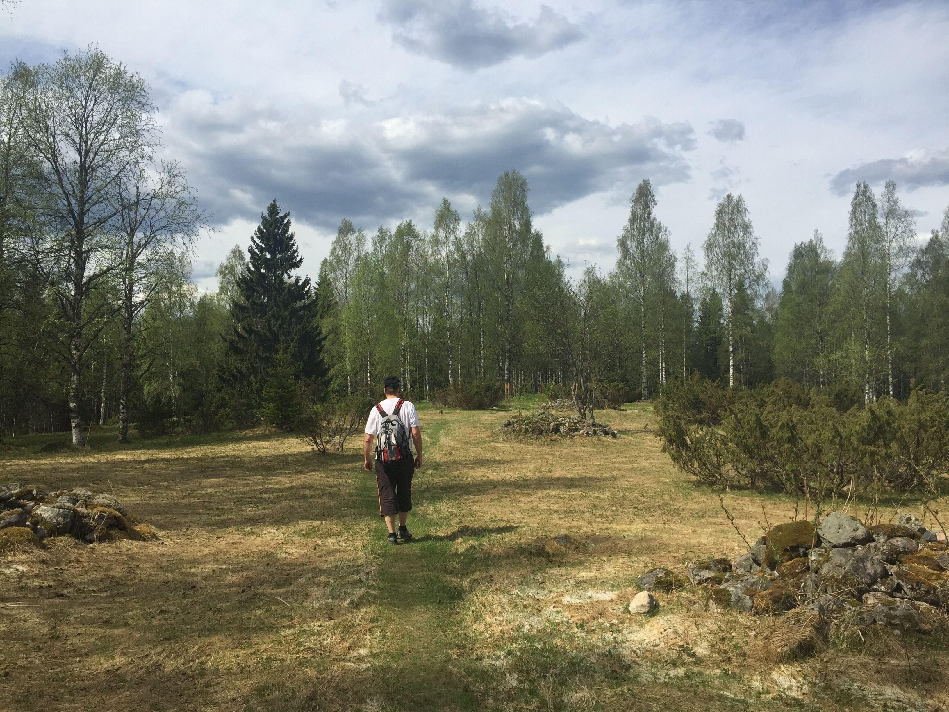 Una persona caminando por un sendero de tierra en un área boscosa con árboles y rocas.