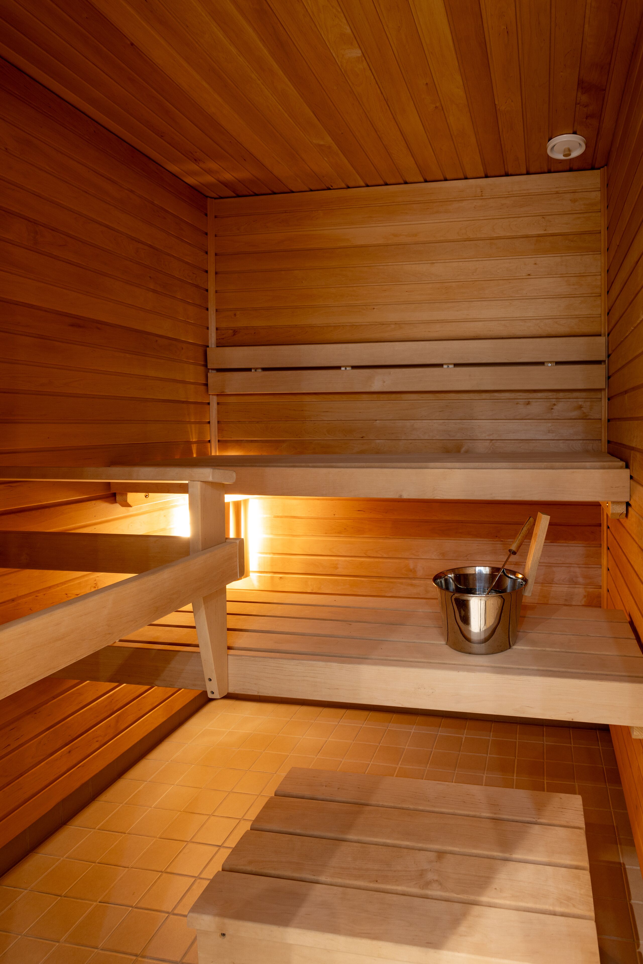 A wooden sauna with benches and a metal bucket.