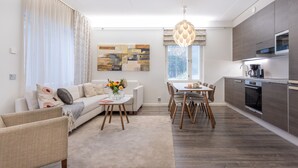A modern living room with a sofa, coffee table, and dining area. There is a kitchen with a microwave and oven. - Vuokatti Booking Suites   (Sotkamo)