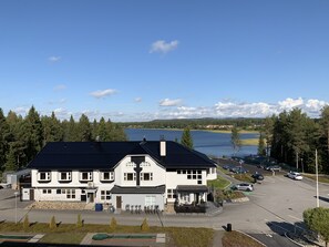 A large building with a swimming pool in front, surrounded by trees and a lake. - Vuokatti Booking Suites   (Sotkamo)