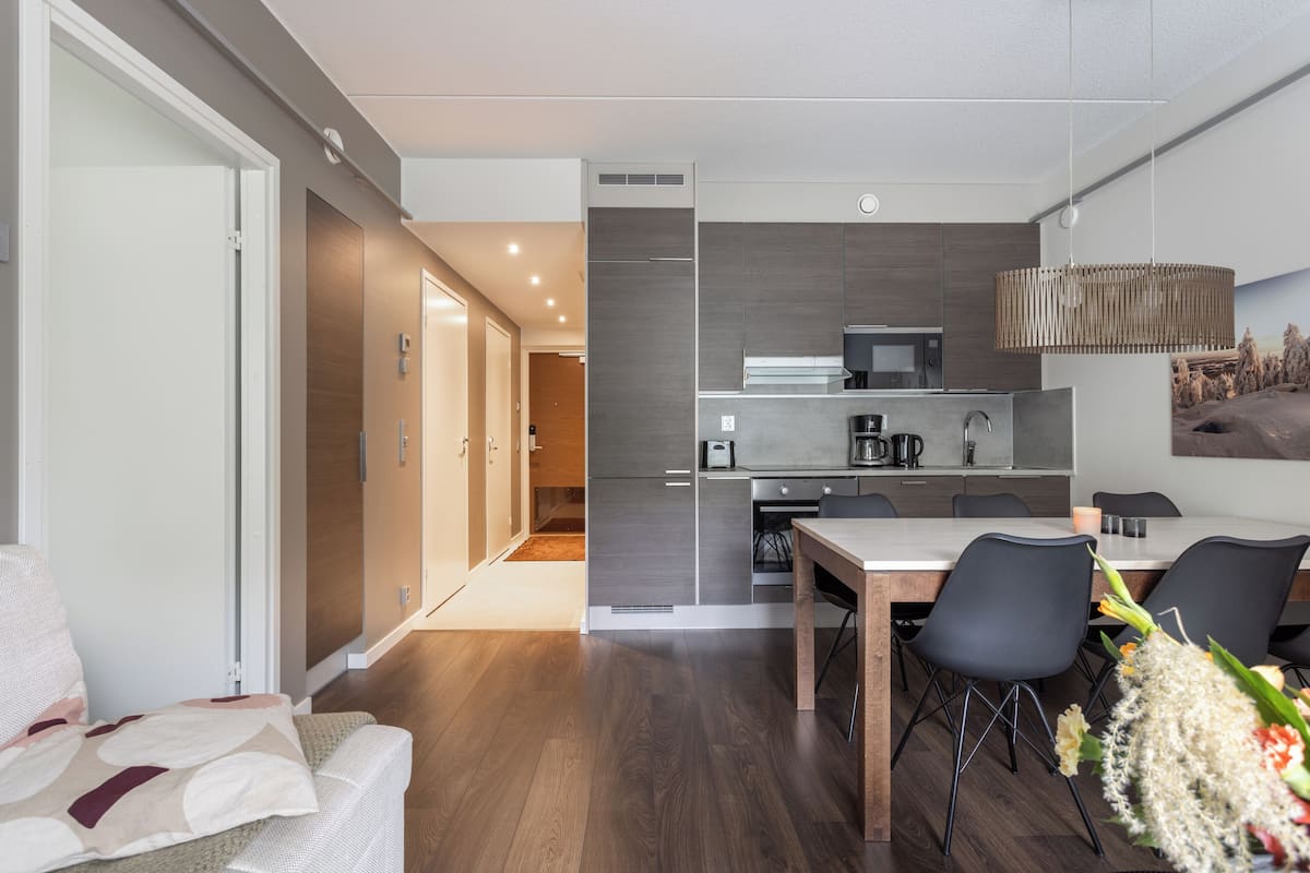 Eine moderne Küche mit Essbereich, ausgestattet mit einem Holztisch, Stühlen, einem Kühlschrank und einer Pendelleuchte.