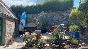 Un bâtiment en pierre, avec une planche de surf, des sièges en plein air et des plantes en pot.