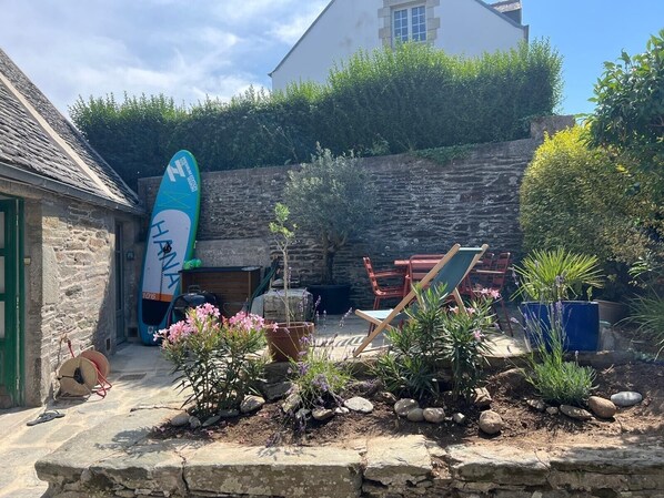 A stone building with a surfboard, outdoor seating, and potted plants.