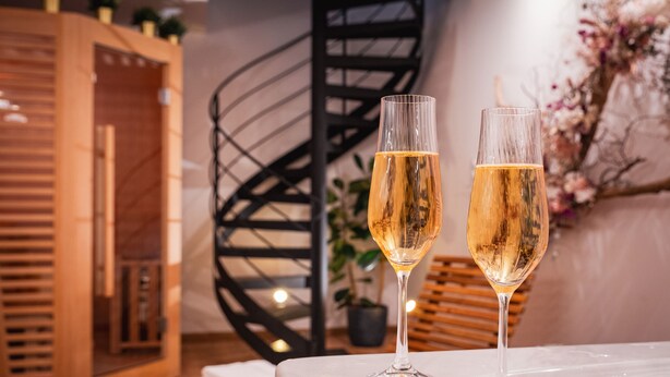 Two glasses of champagne on a table in a room with a spiral staircase and wooden decor.