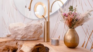 A bathroom with a gold faucet, a vase with flowers, and a wooden surface.