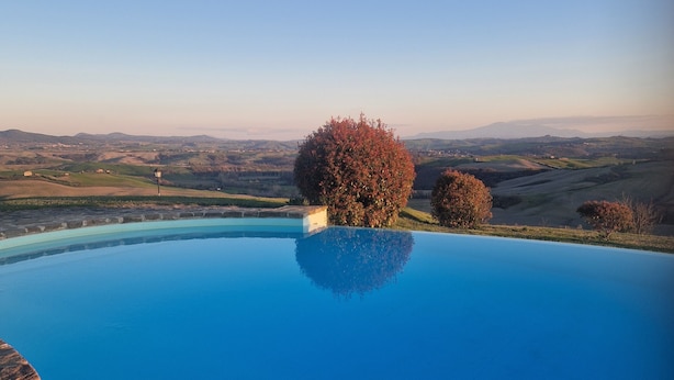 Una piscina infinita azul cristalina, con borde de piedra, rodeada de árboles y vistas a colinas onduladas.