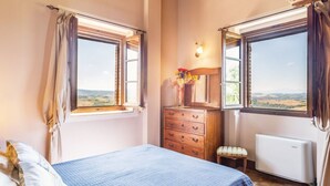 Un dormitorio con cama, cómoda y dos ventanas con vistas.