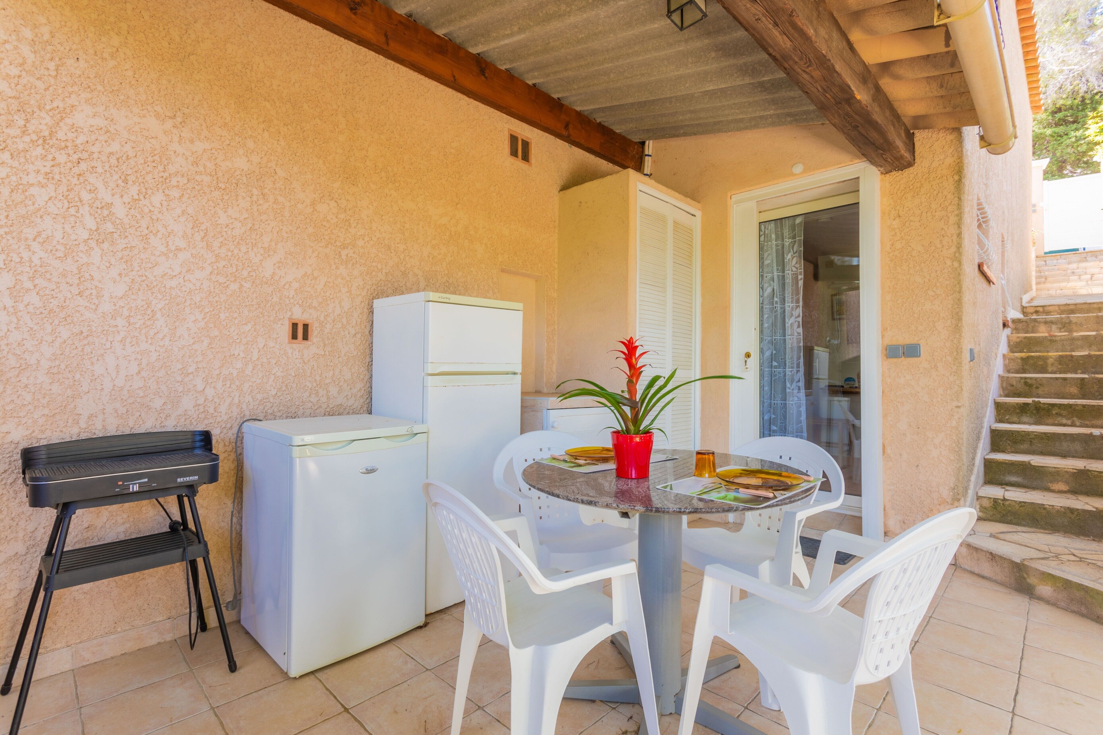 A small outdoor kitchen area with a refrigerator, a portable grill, and a dining table with chairs.