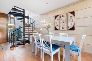 A dining area with a white table, blue cushioned chairs, a vase with flowers, and a wall clock.