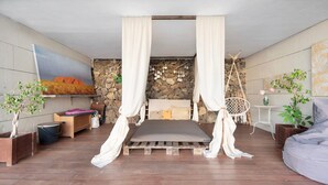 A room with a bed, a TV, a stone wall, a wooden floor, and a hanging chair.