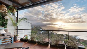 A balcony with a view of the sea, potted plants, and a blue sofa.