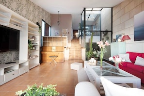 A modern living room with a TV, white furniture, a red sofa, and a staircase leading to an upper level.