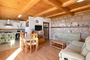 A wooden ceiling, a kitchen with a microwave, a dining table with chairs, a sofa, and a television.