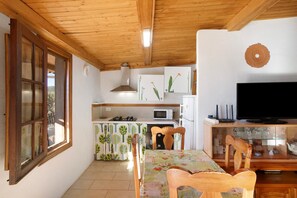 A kitchen with a microwave, stove, and cabinets, a dining area with a table and chairs, and a TV on a wooden stand.