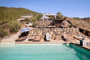 Un espace piscine avec des chaises longues, un mur en pierre et une vue sur une colline.