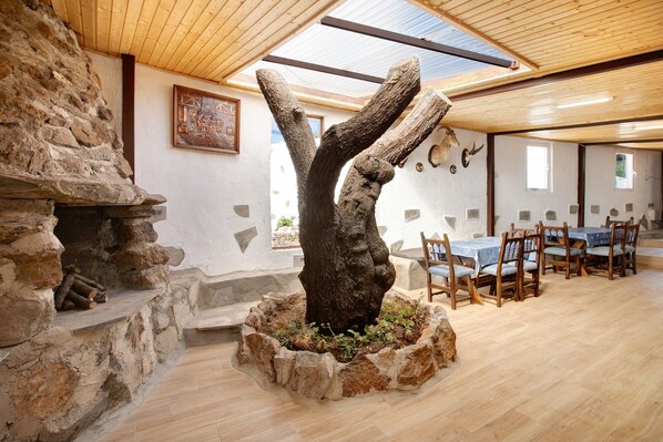 A rustic interior with a stone fireplace, a wooden dining area, and a large tree sculpture.
