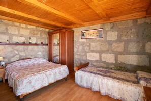 Um quarto com duas camas, vigas de madeira no teto, paredes de pedra, um guarda-roupa de madeira e um quadro na parede.