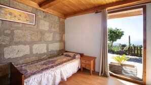 A room with a wooden ceiling, a bed with a floral bedspread, a wooden nightstand, and a view of the outdoors through a glass door. - Vacation Home "El Cazador 2" with Sea View, Shared Pool & Wi-Fi (granadilla)