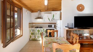 A kitchen with a microwave, stove, and cabinets, a dining area with a table and chairs, and a TV on a wooden stand. - Vacation Home "El Cazador 2" with Sea View, Shared Pool & Wi-Fi (granadilla)